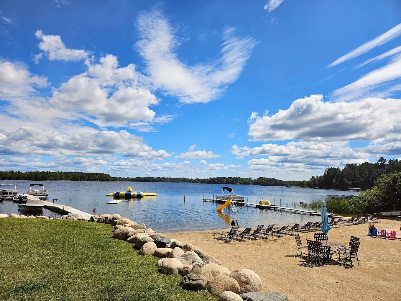 A sandy beach and dock on a calm northern lake under a wide blue sky at Empty Bar Resort